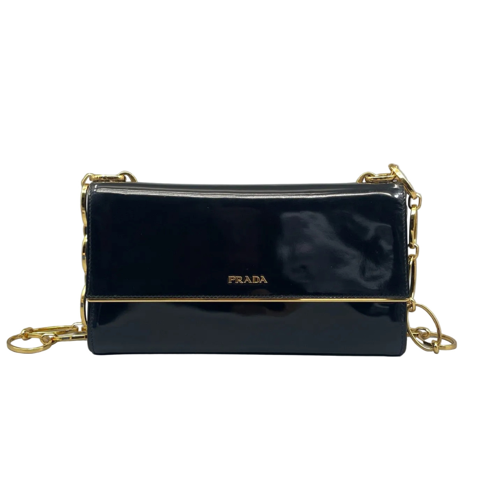 Front view of a Prada flap shoulder bag in shiny black Spazzolato patent leather, featuring a gold-tone Prada logo and a decorative gold-tone chain strap against a white background.