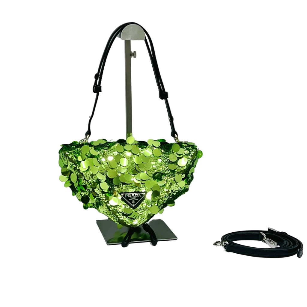 Front view of a Prada Triangle shoulder bag covered in emerald green sequins, featuring the enameled triangle logo, silver-tone hardware, and a detachable chain strap on a white background.