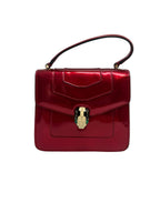 Front view of a Bvlgari Serpenti Forever top-handle bag in metallic ruby red leather with iconic enamelled snake head closure.