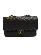 A black quilted flap shoulder bag with gold-tone hardware, featuring a prominent interlocking CC turn-lock and a chain strap, photographed against a neutral light gray background.