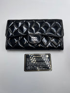 Front view of a Chanel Classic Flap Wallet in black quilted patent leather with silver CC logo emblem and authenticity card.