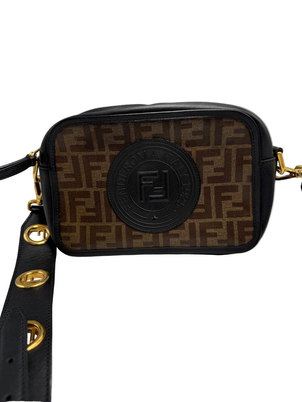 Front view of a Fendi camera bag in brown FF Zucca tapestry canvas with black leather trim, circular logo patch, and wide gold eyelet strap.