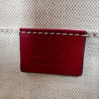 Close-up of a Gucci leather patch with 'GUCCI made in Italy' embossed on it, attached to a beige woven canvas bag.