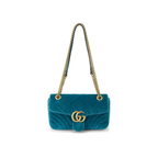 A teal velvet shoulder bag with a gold-tone interlocking G logo on the front and a gold chain strap, shown against a plain white background.