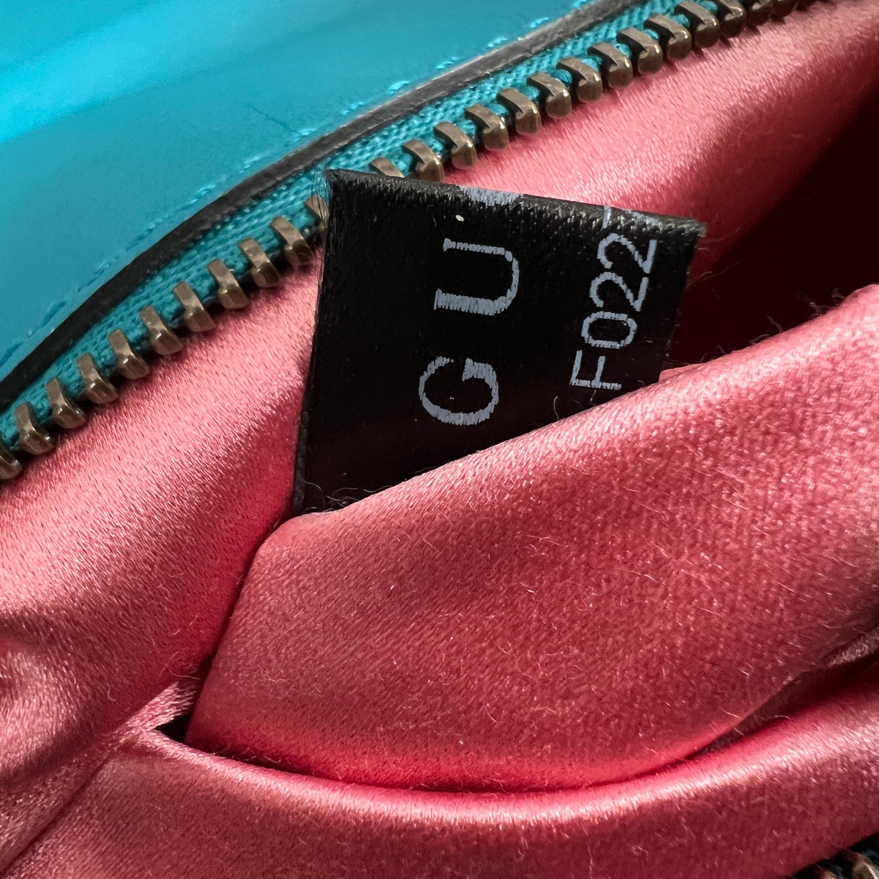 Close-up of a handbag interior showing a pink satin lining, a turquoise blue exterior zipper, and a black fabric label with white text.