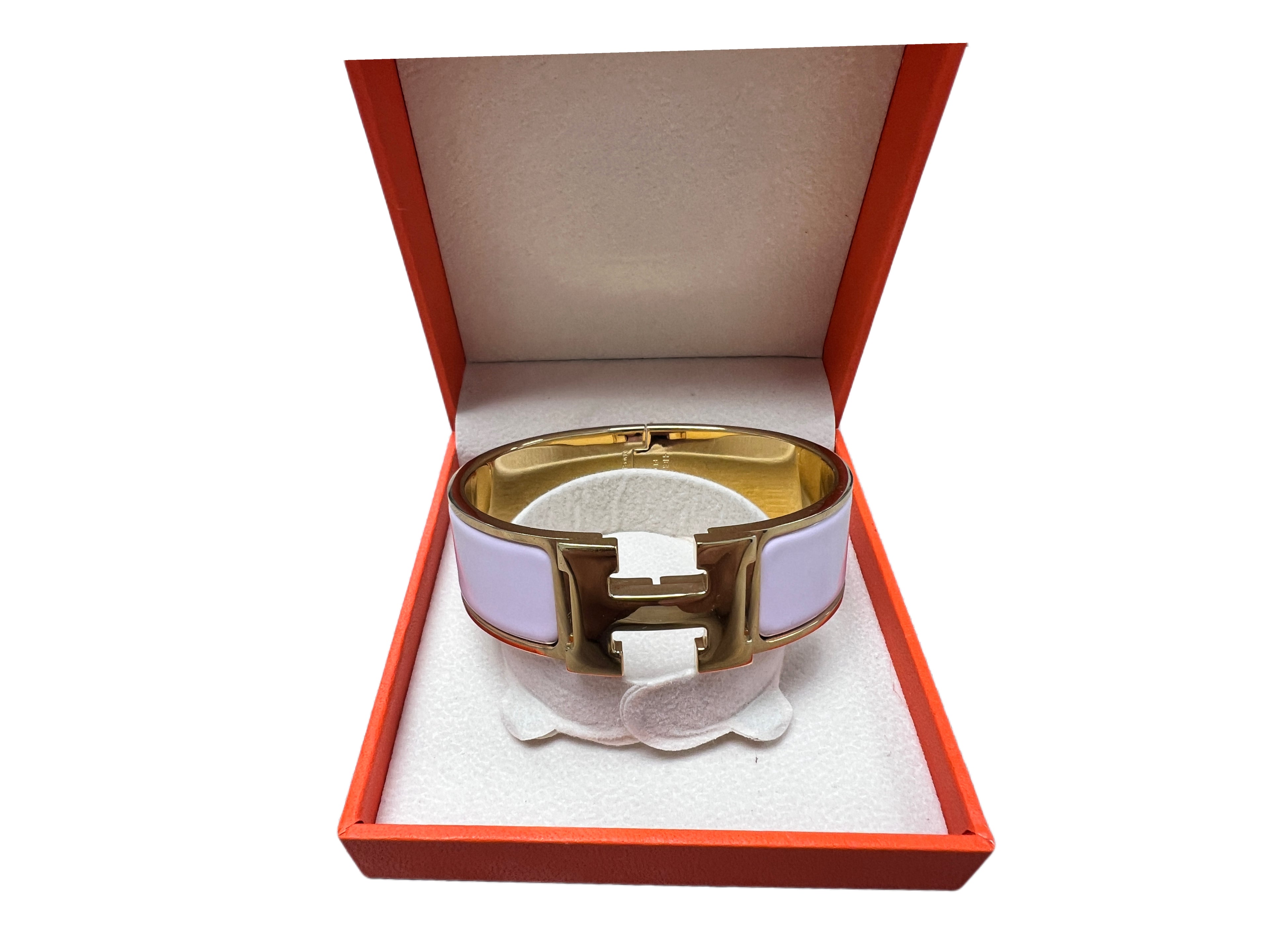 Front view of a Hermès Clic Clac H wide enamel bracelet in pale pink and gold hardware displayed inside an orange Hermès box.