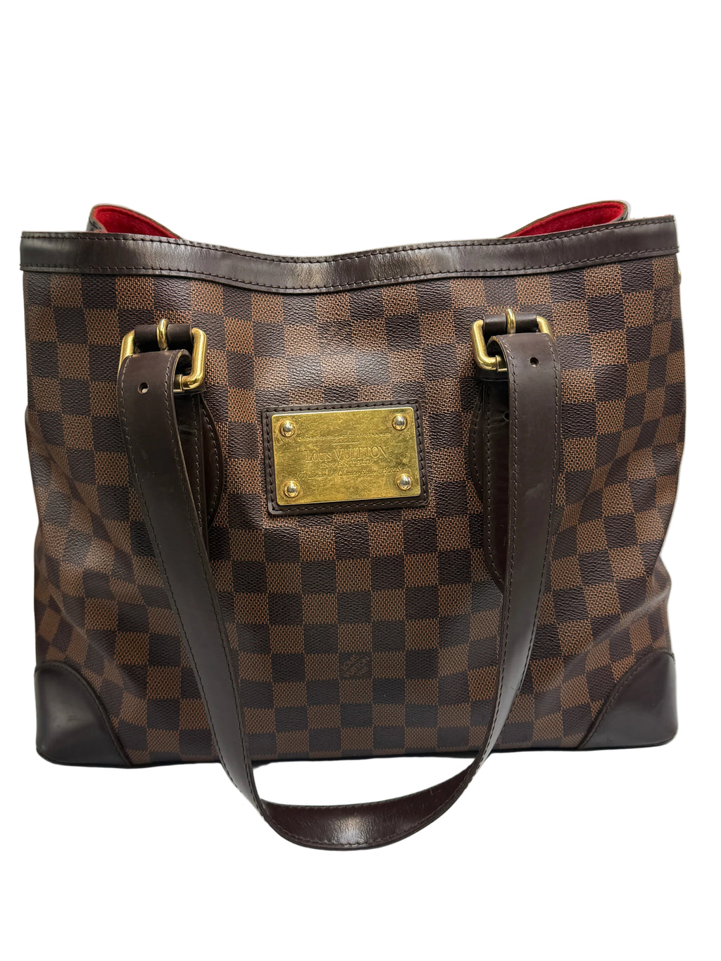 A Louis Vuitton Damier Ebene canvas tote bag with a brown checkerboard pattern, dark brown leather trim, gold-tone hardware, and a red interior lining, shown against a neutral light gray background.