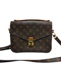 A Louis Vuitton monogram canvas shoulder bag in dark brown with gold-tone hardware and a top handle, shown against a neutral gray background.