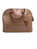 A Louis Vuitton dome-shaped handbag in glossy beige patent leather with the embossed monogram pattern, gold-tone hardware, dual top handles, and a hanging leather tag, photographed against a neutral gray studio background.