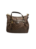 A Louis Vuitton handbag in the Damier Ebene checkered pattern, featuring brown leather handles and gold-tone hardware, set against a neutral gray background.