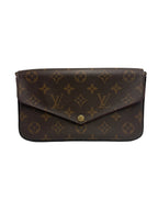 A Louis Vuitton monogram canvas clutch bag in dark brown with gold-tone hardware, photographed against a neutral light gray background.