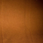Close-up of a warm brown suede or microfiber fabric surface with visible stitched seam lines and a small portion of a metallic zipper at the top left.