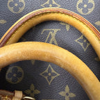 Close-up of a Louis Vuitton monogram canvas bag with a curved tan leather handle, showing the classic dark brown and beige LV pattern.
