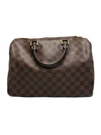 A brown checkered leather handbag with dark brown handles and gold-tone hardware, photographed against a neutral gray background.