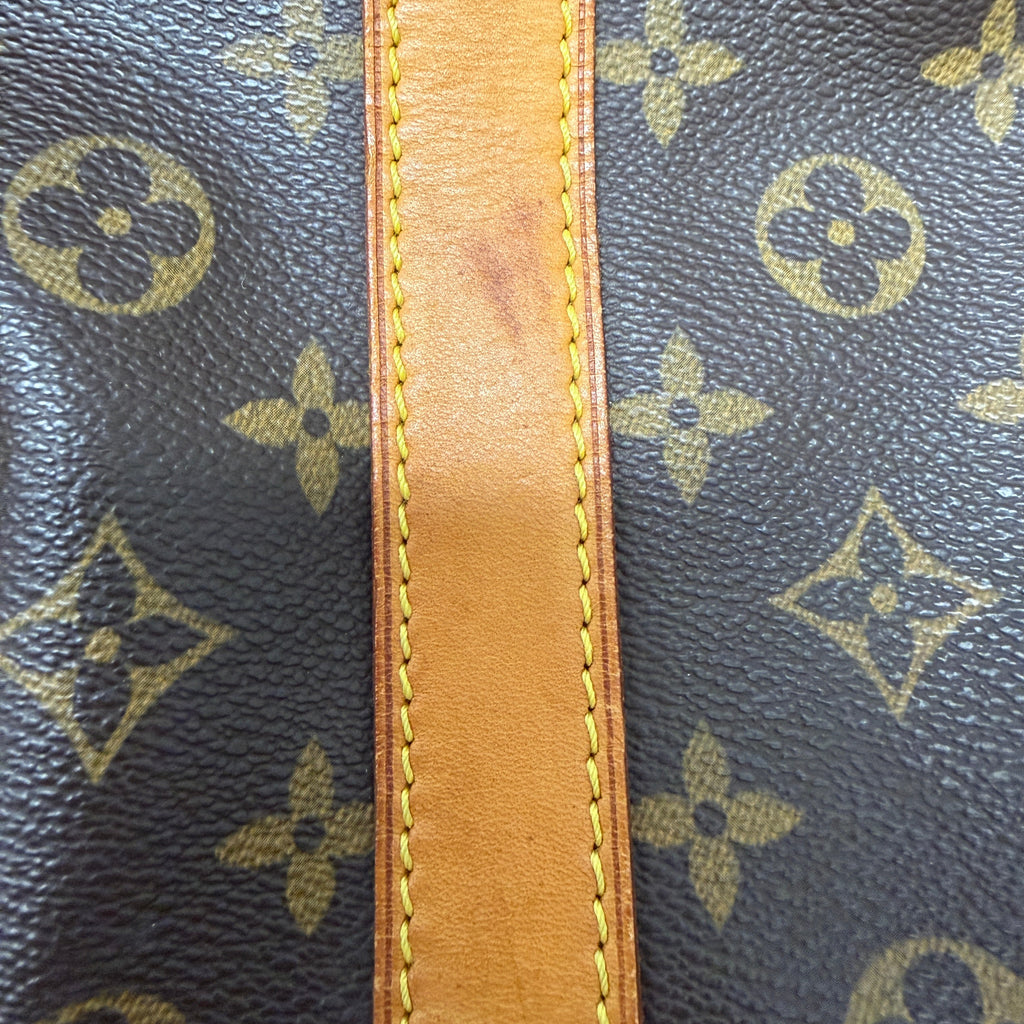Close-up of a Louis Vuitton monogram canvas bag with a tan leather trim and visible scuffing on the leather strip.