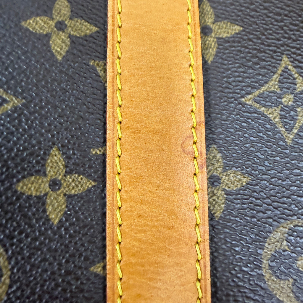 Close-up of a Louis Vuitton monogram canvas bag with a tan leather trim and yellow stitching.