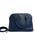 Front view of a Prada Promenade dome satchel in dark navy blue Saffiano leather with gold-tone hardware and matching adjustable strap.
