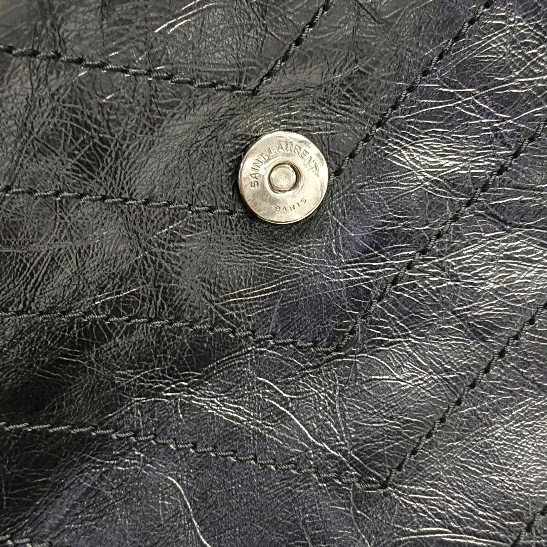 Close-up of a black leather saint laurent niki medium with a brand logo on a textured surface